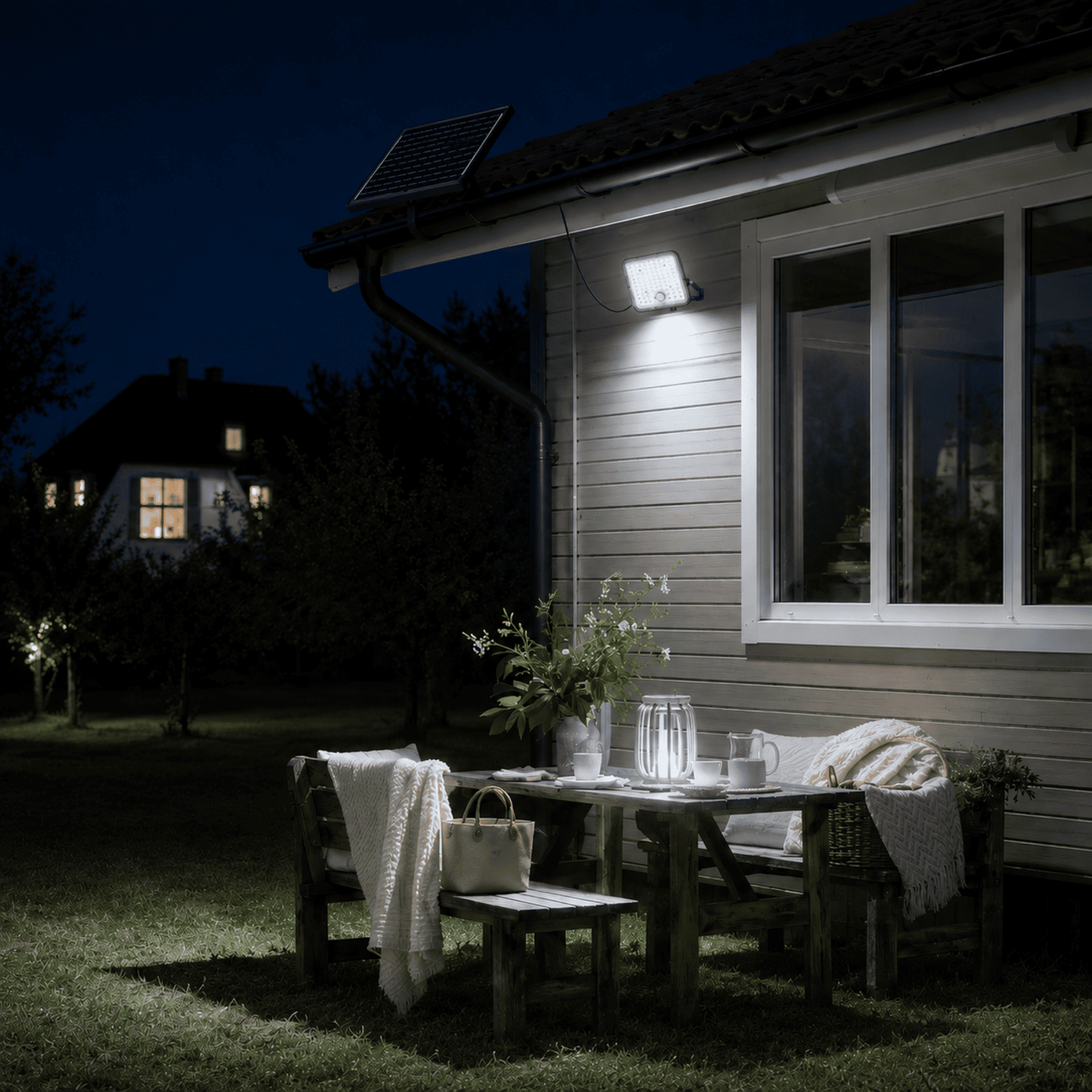 Proyector Solar LED SenseLight 100W iluminando un jardín con sensor de movimiento PIR durante la noche.